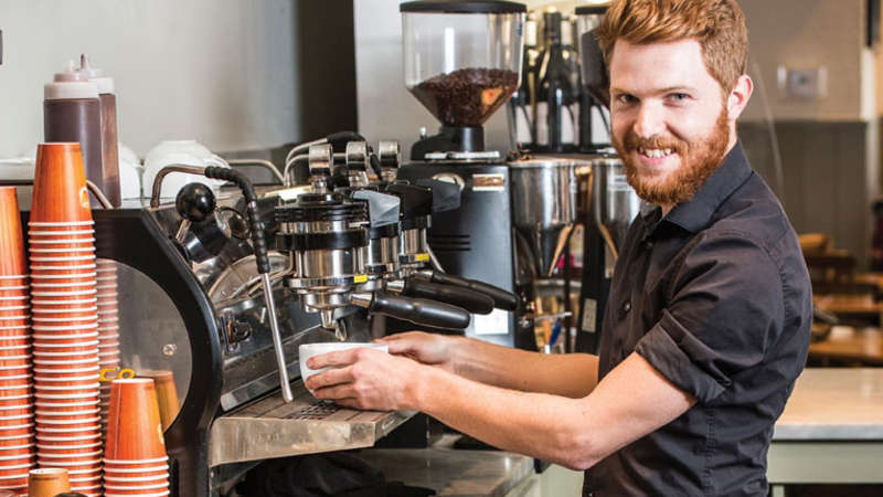 Barista przygotowuje napój przy ladzie kawiarni
